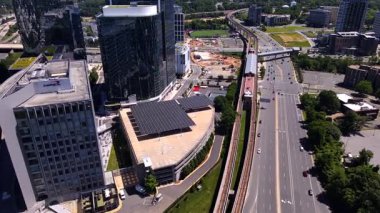 Gökdelenler, çatılardaki güneş panelleri, otoyol ve metro istasyonları. Kamera metro hattı boyunca hareket ediyor..