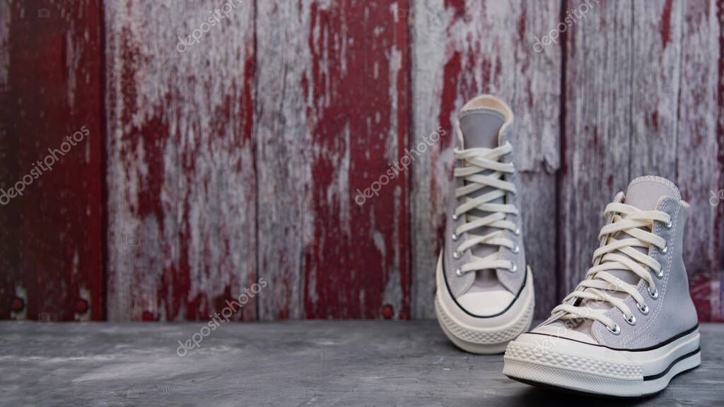 Urban Casual Vibes. Gray canvas shoes placed on textured red wood background.