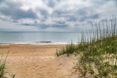Atlantik Okyanusu 'nun üzerinde mavi bulutların altında çimenli kıyı kum tepeleri.