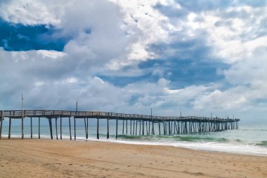 Kumlu sahil şeridinde balıkçı iskelesi. Huzurlu deniz manzarası, okyanus dalgaları ve dramatik bulutlar..