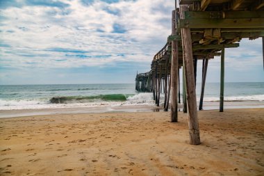 Geniş kıyı şeridindeki Rustik ahşap iskele. Bulutlu yaz gökyüzü sakin deniz ve boş sahil üzerinde.