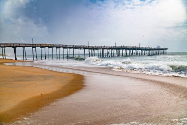 Kumlu sahil şeridinde balıkçı iskelesi. Huzurlu deniz manzarası, okyanus dalgaları ve dramatik bulutlar.