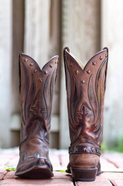 Tuğla kaldırımda yıpranmış bir ağaca karşı deri kovboy çizmeleri. Amerikan kovboy kültürü..