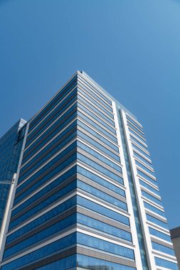 Mavi gökyüzüne karşı modern cam gökdelen. Yansıtıcı pencereleri ve gösterişli mimarisi olan büyük bir ofis binası..