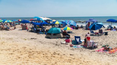 Tatilciler okyanus kıyısındaki kumlu sahilde güneşleniyor.
