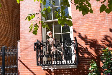 Korkutucu ama etkileyici bir Cadılar Bayramı dekoru. İskelet, kırmızı tuğlalı evin eski demir balkonundan misafirleri selamlıyor..
