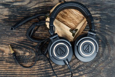 Ses-Teknik M-serisi kulaklıklar, klasik stil ve sarmalanmış kablolar. Stüdyo kalitesinde ses ekipmanları deri çantanın yanında dokulu ahşabın üzerinde dinleniyor..