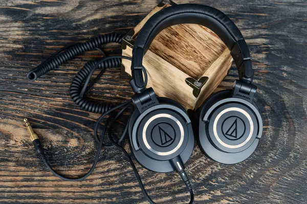 Ses-Teknik M-serisi kulaklıklar, klasik stil ve sarmalanmış kablolar. Stüdyo kalitesinde ses ekipmanları deri çantanın yanında dokulu ahşabın üzerinde dinleniyor..