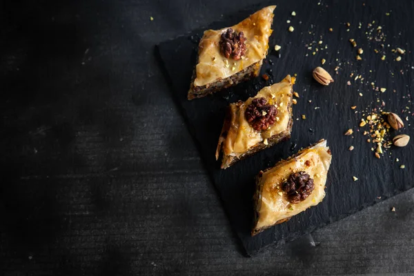 stock image Homemade baklava with pistachios and walnuts and honey and orange syrup served in a black plate. Turkish culture Turkish cuisine. Place for text