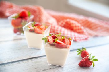 Çilek soslu vanilyalı panna cotta ve cam bardaklarda çilek arkaplanda kareli peçeteyle. Ev yapımı tatlı.