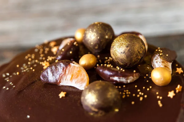 暗い木のテーブルの背景に金のチョコレートボールやキャンディーやみかんで飾られたハッピー大晦日のチョコレートケーキ 閉じろ — ストック写真