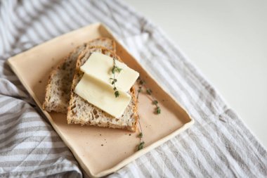 Keten kumaşın üzerinde seramik bir tabakta tereyağı ve kekik filizi ile bir somun ekmek. Noel ağacının odaksız ışıkları. Tatil havası. Noel ve Mutlu Yıllar.