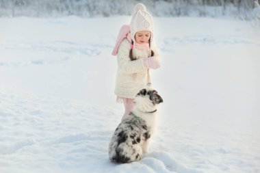 Kışın kar üzerinde arkadaşı Avustralya çoban köpeğiyle oynayan bir kız. Güzel, buzlu ormanın yanında. Çocuk ve köpeğin arkadaşlık kavramı