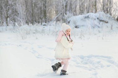 Beyaz kürklü ve pembe örülü eşarplı mutlu küçük kız güzel bir kış ormanında oynar. Noel havası