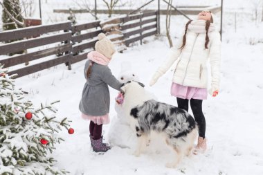 Rahibeler, Avustralya çoban köpeği ve kış bahçesinde pembe örülü eşarplı bir kardan adamla oynuyorlar. Açık havada süslenmiş Noel ağacı