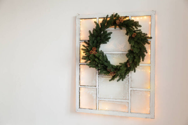 Christmas green wreath with cones on the window in a holiday studio