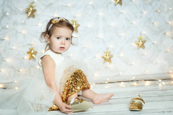 白と金のドレスにかわいい赤ちゃんの女の子の肖像画や星やライトでゴールデンスパークリー背景に小さな光沢のある靴を着て 魔法のクリスマスタイム — ストック写真