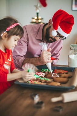 Baba Noel Baba şapkası ve küçük kızı zencefilli Noel kurabiyesi süslüyor.