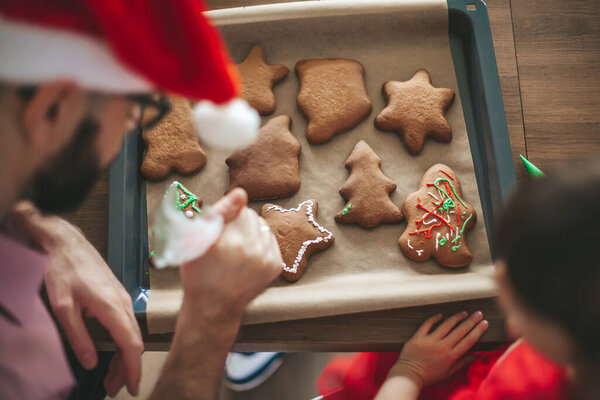 Отец и его маленькая дочь украшают пряничное рождественское печенье, вид сверху 