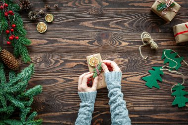 Köhne bir Noel kompozisyonu yatıyordu, elleri küçük bir hediye kutusu dekore ediyordu, köknar dalları ve kahverengi ahşap arka planda Noel süslemeleri vardı.
