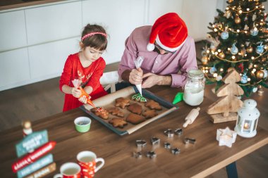 Babası ve küçük kızı zencefilli çörekleri Noel kurabiyeleriyle süslüyor.