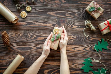 Çevre dostu Noel kompozisyonu. Elleri ahşap bir arka planda küçük bir hediye kutusu tutuyor.