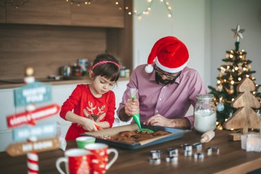 Sevimli küçük kız ve babası mutfakta zencefilli kurabiye süslüyor. Noel ve Yeni Yıl Hazırlığı.