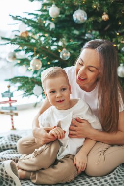 Sevimli küçük çocuk ve annesi evdeki süslü Noel ağacının yanında oturuyorlar. Aileyle yeni yıl tatili.