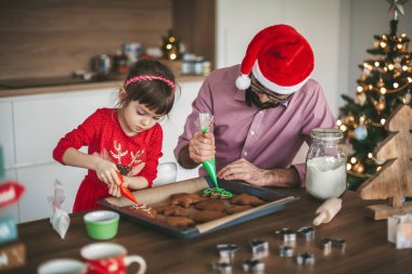 Tatlı küçük kız ve babası zencefilli Noel kurabiyesi dekore ediyorlar.
