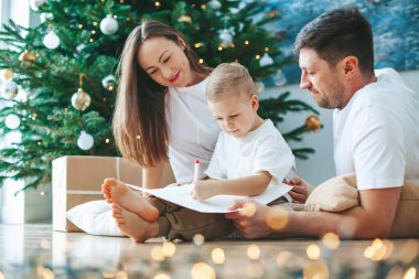 Ailesi Noel Baba 'ya mektup yazan sevimli küçük bir çocuk. Aile, Noel ağacının yanındaki hediyelerle ilgili rüyalar yazıyor. Mutlu Noeller ve mutlu yıllar.!