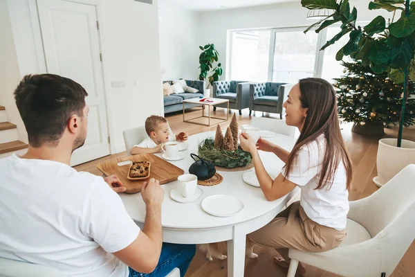 圣诞节的早晨 一家人在家里坐在餐桌旁 幸福极了 爸爸和他们的小儿子喝茶 吃蛋糕当圣诞早餐 — 图库照片