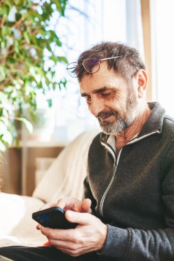 Olgun bir adam kanepeye oturmuş, mesajlaşıyor, arıyor ya da modern bir akıllı telefondan kitap okuyor. Teknoloji kavramını kullanan yaşlılar.