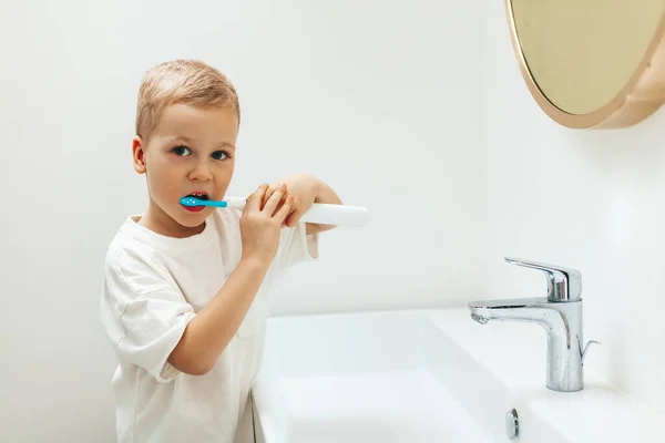 Little boy brushing teeth with electric toothbrush in front of the sink in a bathroom. Dental hygiene and heath for children.