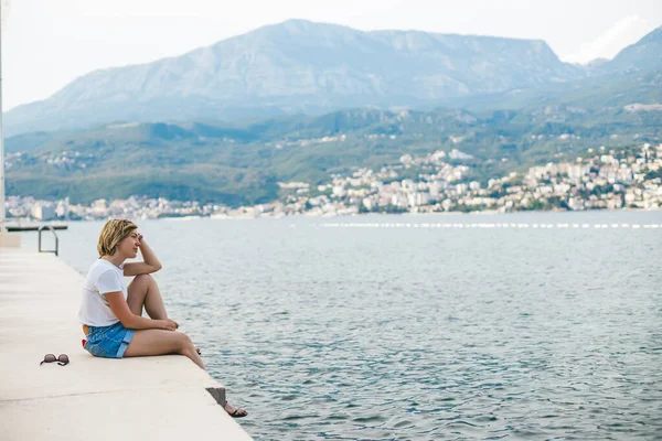 Relaxing woman sitting on the edge of a pier, enjoying beautiful view of Boka-Kotor bay in Montenegro