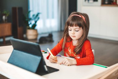 Cute little girl learning art lesson online on a tablet. Virtual drawing painting class. Modern homeschool study.