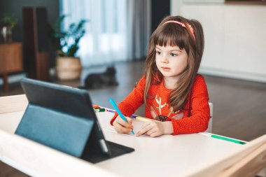 Cute little girl learning art lesson online on a tablet. Virtual drawing painting class. Modern homeschool study.