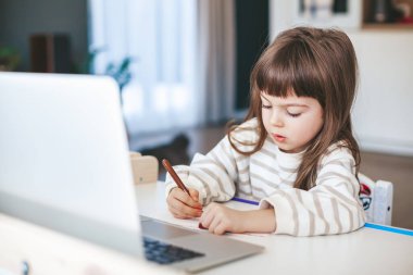 Cute little girl learning art lesson online on a laptop. Virtual drawing painting class on video. Distant remote video education. Modern homeschool study.