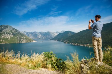 Akıllı telefonuyla resim çeken turist, bir uçurumun kenarında duruyor, Karadağ 'ın Kotor Körfezi' nin muhteşem deniz manzarasının tadını çıkarıyor.