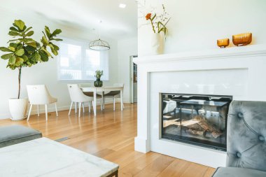 Zarif beyaz yemek odası ve oturma odası. Masanın yanında büyük bir çiçek ve kanepenin yanında sıcak bir şömine.