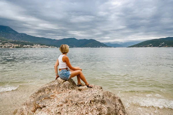 在多云的天气里 女人坐在一块大石头上 欣赏黑山博卡 科托尔湾的美丽景色 — 图库照片