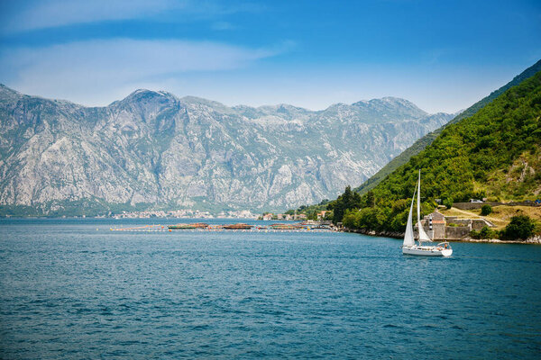 View of famous Bay of Kotor and a floating white yacht on a beautiful sunny day, Montenegro