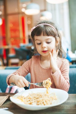 Lokantada soslu spagetti yiyen tatlı küçük kız.