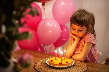 Tatlı düşünceli küçük kız doğum günü pastasına bakıyor, dilek diliyor.