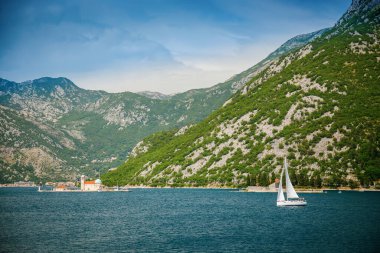Kayalıkların Leydisi Kilisesi 'nin ve Kotor Körfezi' nde güneşli bir yaz gününde yüzen beyaz bir yatın görüntüsü, Karadağ