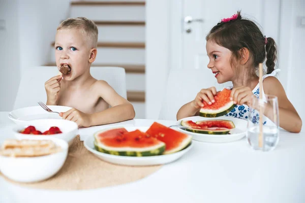 2人の子供が家で新鮮なジューシーなスイカとアイスクリームを食べる — ストック写真