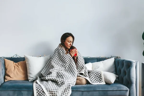 Peaceful scene of a woman on the couch, savoring a warm drink under her cozy blanket