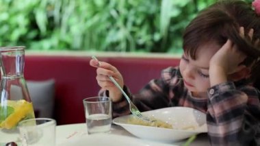 Sevimli kız 5-6 yaşlarında, rahat bir kafede peynirli spagetti yiyor.