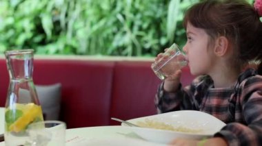 5-6 yaşlarında, kafede yemek yerken su içen çekici bir kız.
