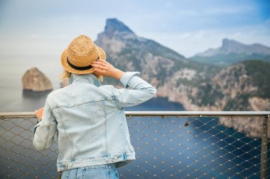 Hasır şapkalı kadın Mallorca, İspanya 'daki Cap de Formentor' a bakıyor.