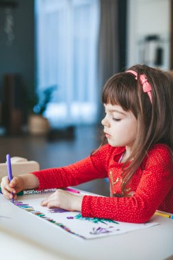Sevimli küçük kız 4-5 yaşlarında keçeli kalemlerle mutlu bir Noel sahnesi çiziyor. Noel atölyesi konsepti.